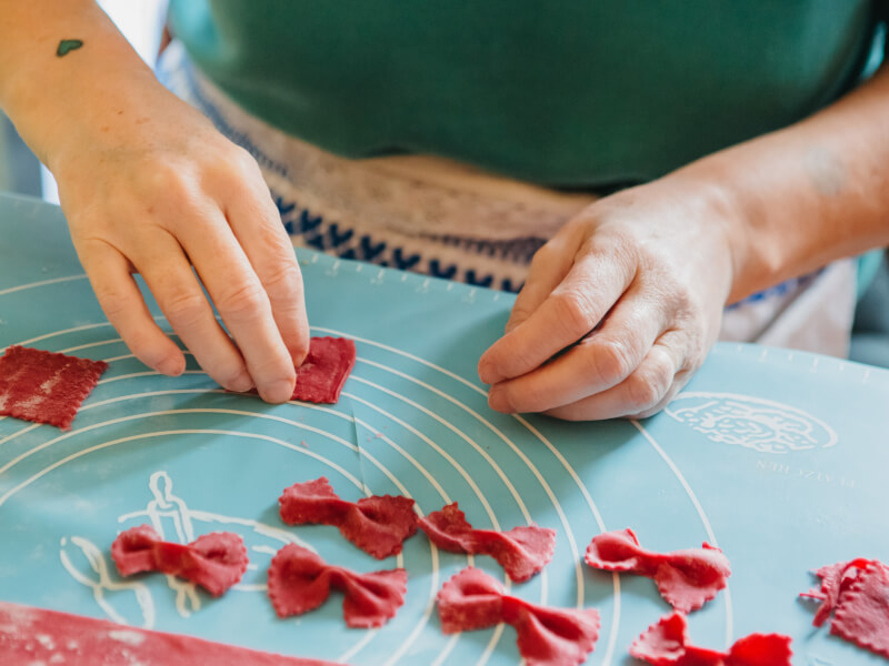 A hand shapes red dough into bow tie shapes at a pasta making class.